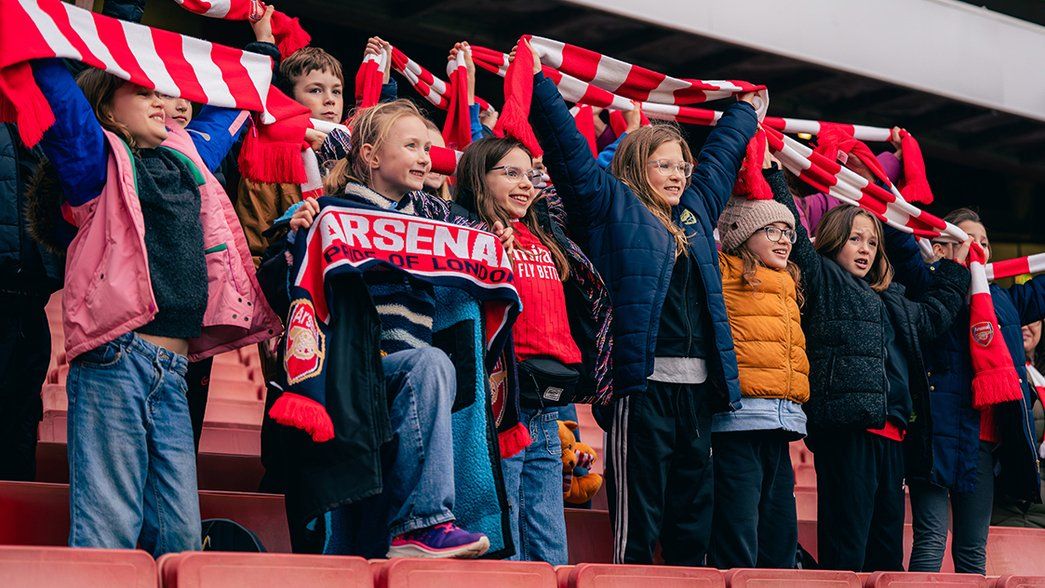 A group of young Arsenal supporters hold up flags in the stands