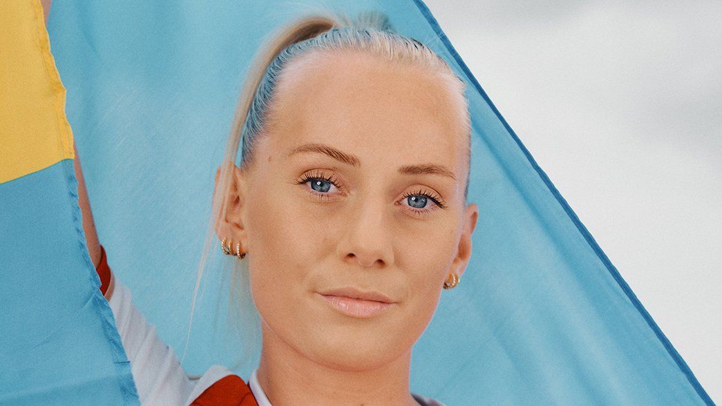 Stina Blackstenius poses behind a Swedish flag in the new Arsenal home shirt